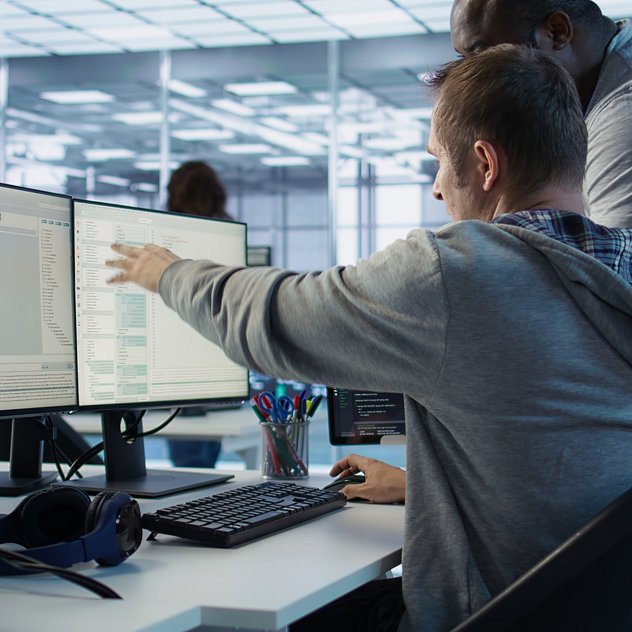 PAVIS Inbetriebnahme von Software: Effizient und Zuverlässig  Zwei Entwickler arbeiten eng an mehreren Monitoren; einer zeigt dem anderen den Code im modernen Büro.